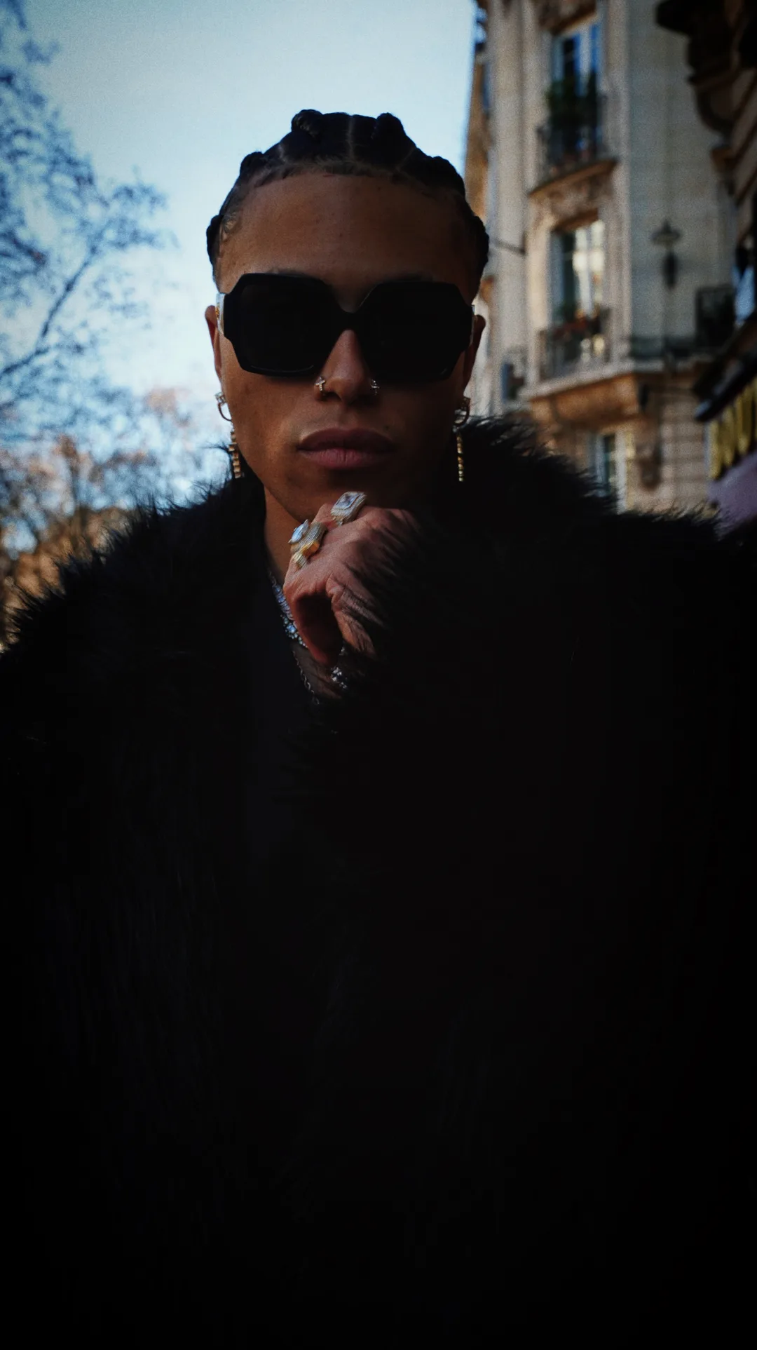 Street portrait in Paris of a person in oversized sunglasses and a black fur coat, jewelled hand raised