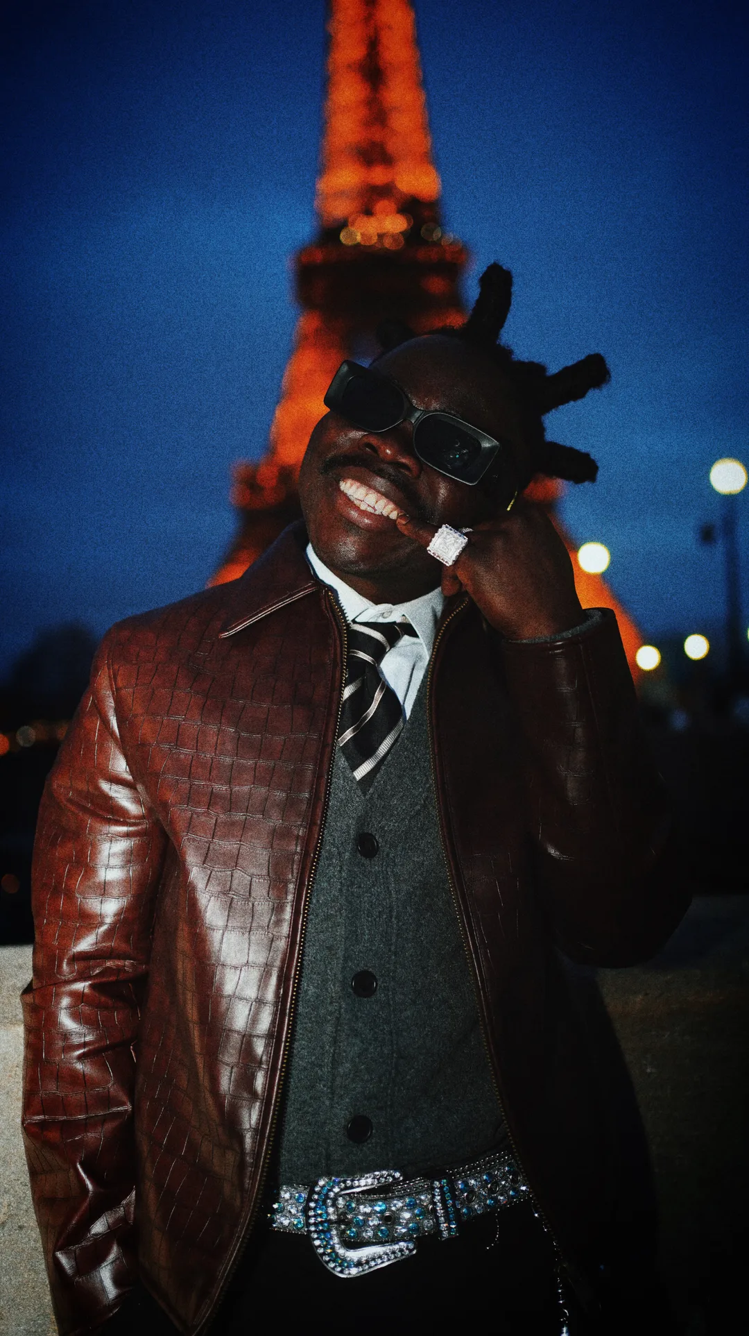 A man in a crocodile-leather jacket and waistcoat in front of the Eiffel Tower at dusk