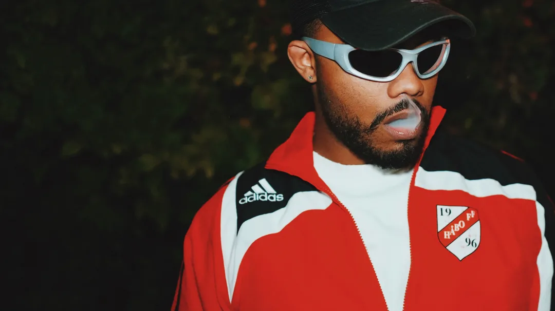 A man in a red track jacket and cap photographed outdoors against soft greenery
