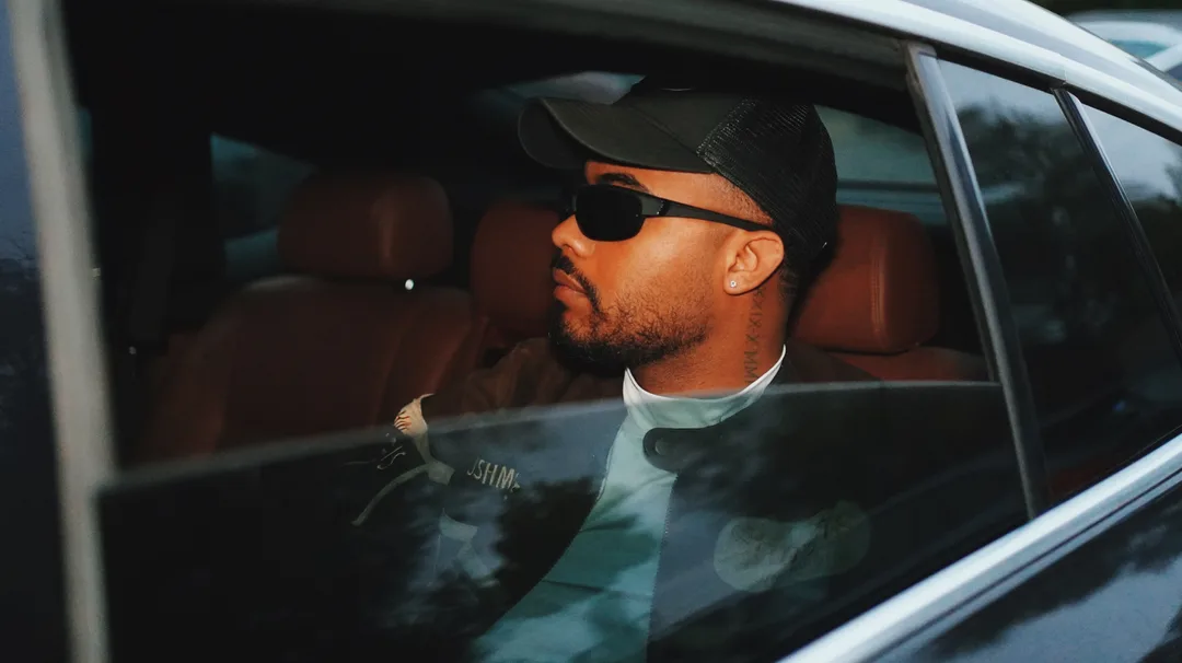A man in a cap and sunglasses seated in a car with a tan leather interior