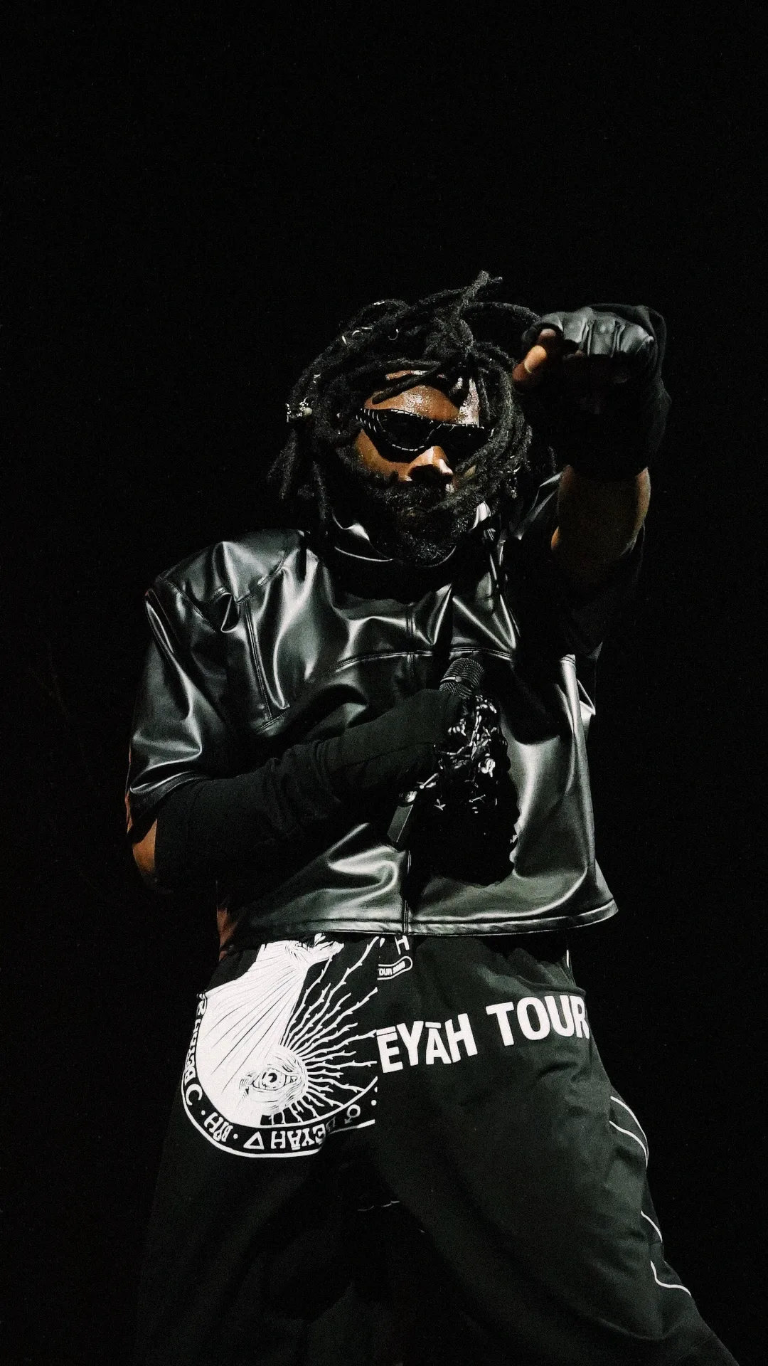 A masked performer on a dark stage wearing a printed tour jersey