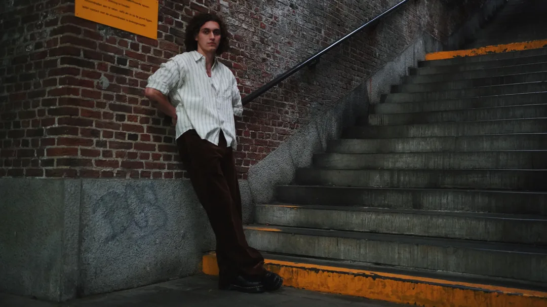 Full-length editorial portrait of a man in a striped shirt on urban concrete stairs