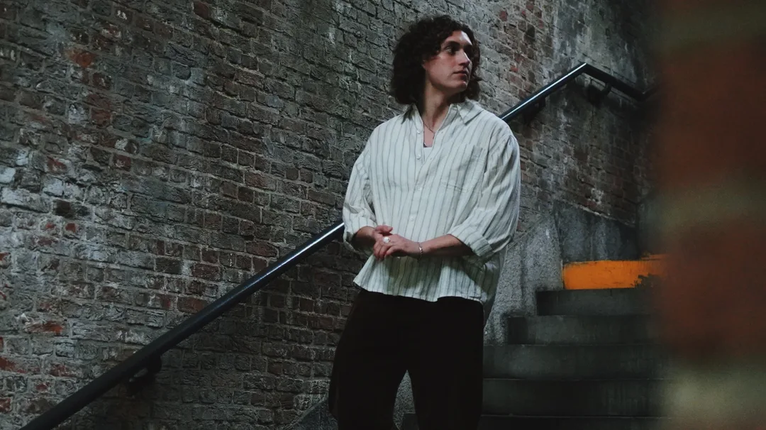 A man in a striped shirt beside a weathered brick wall and metal railing