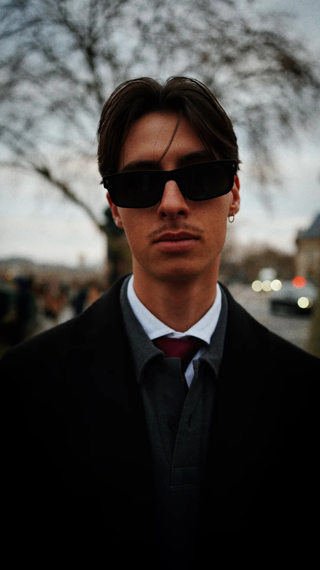 Street portrait of a young man in a dark suit with a red tie and sunglasses