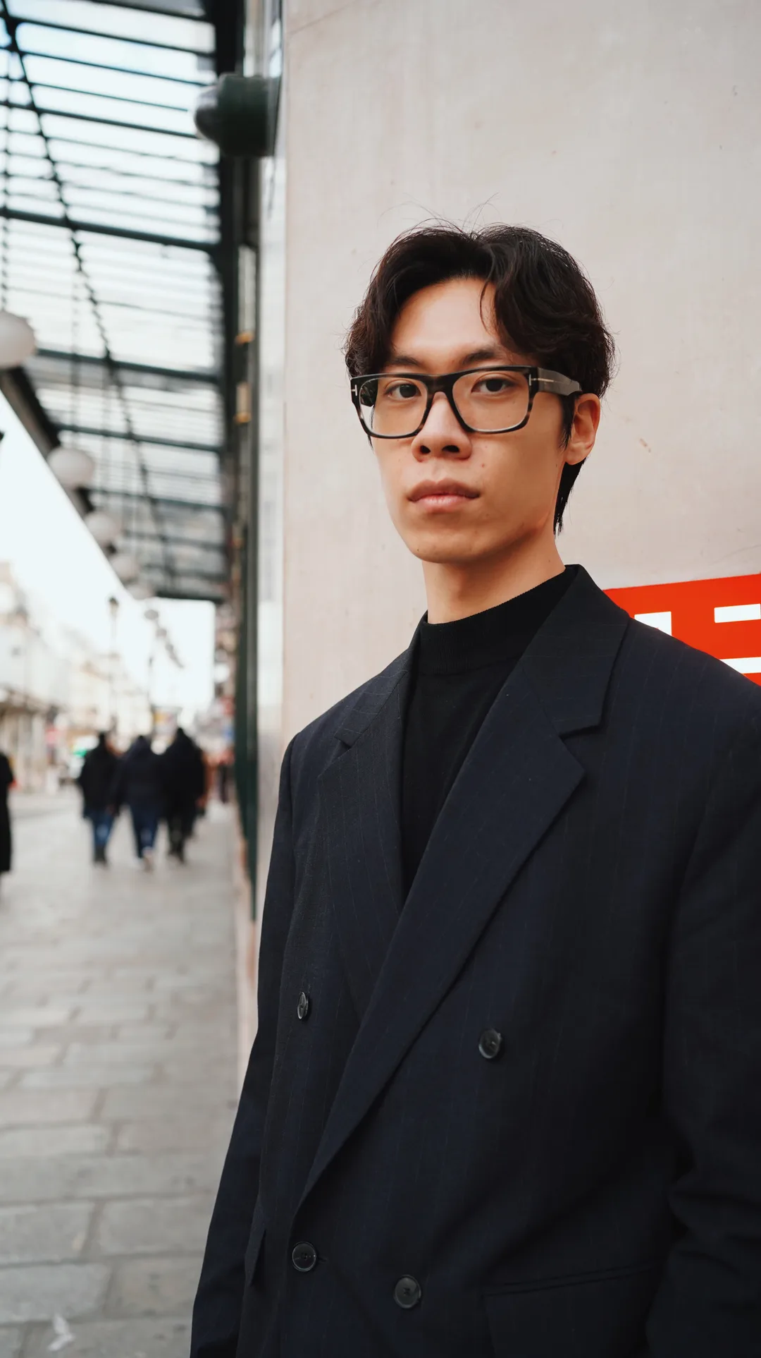 Portrait of a young man in a navy double-breasted blazer and glasses on a city street