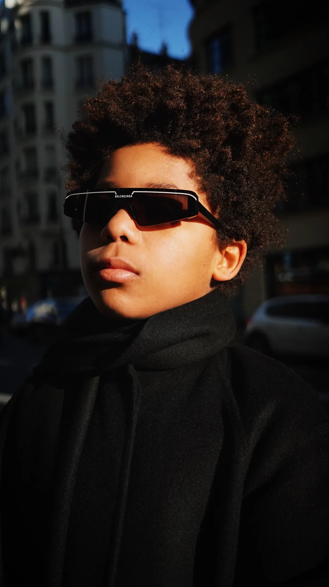 Portrait of a young man with an afro, sunglasses and a black scarf in warm afternoon light