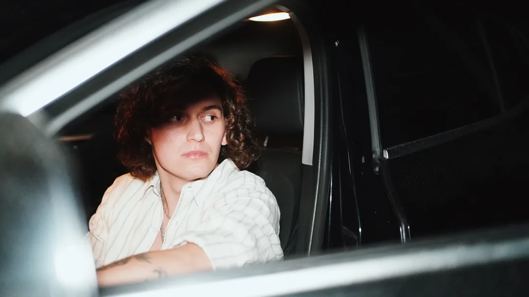 A man with curly hair seated inside a car at night